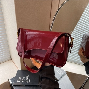 Detail of dark red patent leather shoulder bag with gold hardware and flap closure