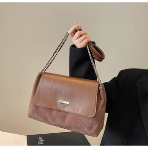 Detail of a brown suede and leather shoulder bag with a silver buckle and chain strap