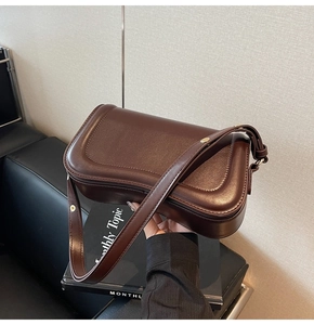 Détail du sac bandoulière marron foncé avec coutures incurvées et boucles dorées chic