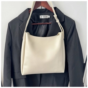 Detail of a beige PU leather tote bag hanging on a black suit jacket for outfit reference