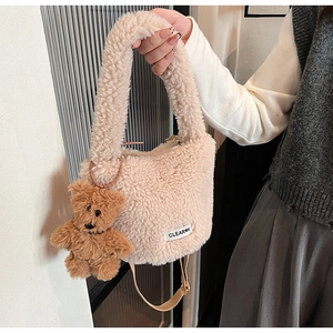Detail view of the plush cream bucket bag featuring a brown teddy bear charm and soft texture