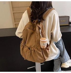 Detail view of a caramel brown nylon backpack featuring side pockets and a cute plush charm