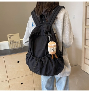 Detail of black nylon backpack featuring large drawstring closure and plush cup charm