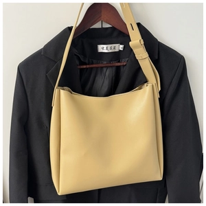 Detail view of beige leather bucket bag featuring a smooth texture and wide shoulder strap