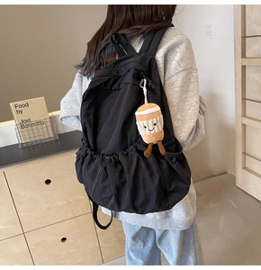 Rear view of black nylon backpack with a plush coffee cup charm in a minimalist room