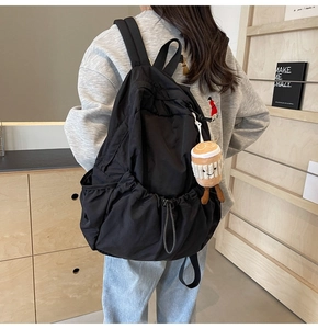 Detail of black nylon backpack featuring drawstring pockets and a cute plush charm