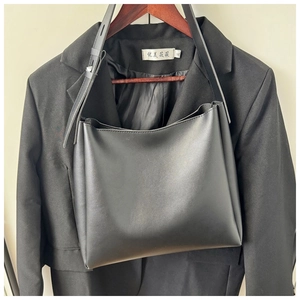 Close-up of black minimalist tote bag on a blazer featuring adjustable strap details