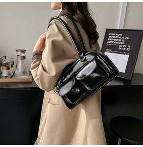 Detail view of glossy black shoulder bag featuring dual front pockets and silver chain accents