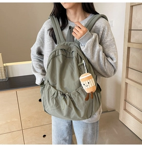Detail of olive green nylon backpack with drawstring front pocket and plush charm