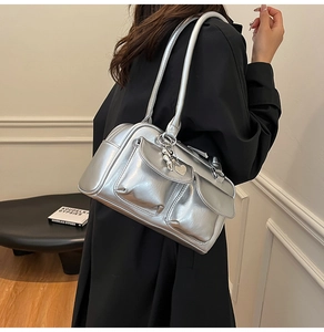 Detail of silver metallic shoulder bag with flap pockets and a heart charm pendant