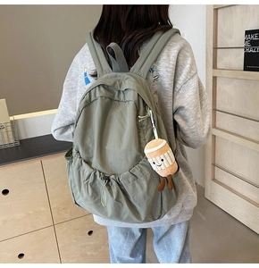 Detail of green nylon backpack with drawstring side pocket and plush coffee cup charm