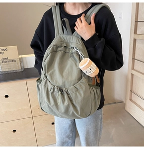 Casual olive green nylon backpack shown on model side-view in a cozy indoor setting