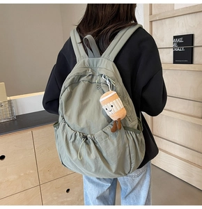 Close-up of a light grey-green nylon backpack with a drawstring pocket and plush charm