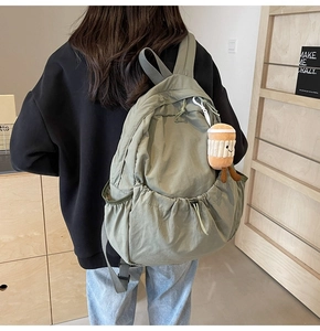 Detail of green nylon backpack with side drawstring pocket and cute coffee cup plush charm