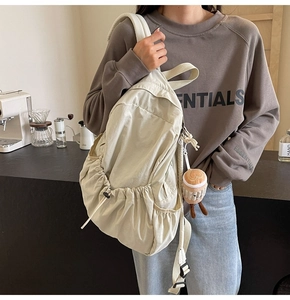 Detail view of cream nylon backpack with side drawstring pocket and cute plush charm