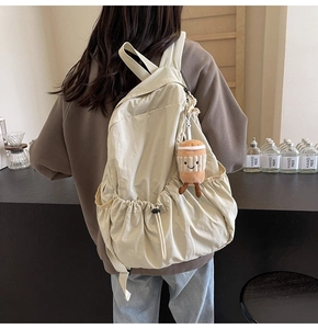 Detail of a beige casual backpack with a cute coffee cup plush charm on the side pocket