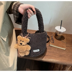 Detail of dark brown plush bucket bag with cute bear charm and woven label on wooden table