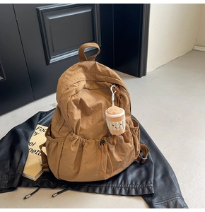 Detail of a brown nylon backpack featuring a creative coffee cup plush pendant on the zipper