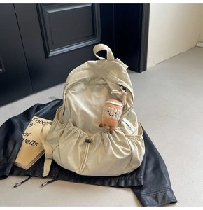 Close-up of cream nylon backpack featuring drawstring pocket and plush cup charm