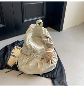 Detail of a cream-white lightweight backpack with a coffee cup plush charm and drawstring