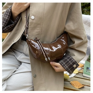 Macro detail of the dark brown patent leather texture and knot design on the croissant bag