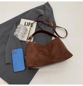Sac hobo en daim marron foncé sur blazer gris avec accessoires de bureau raffinés