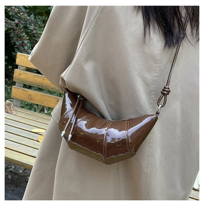 Detail of a brown patent leather croissant bag with pleats and knot strap on a model