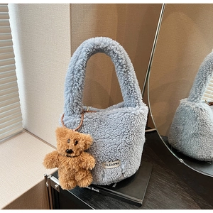 Detail view of a light blue plush bucket bag with a cute brown teddy bear keychain