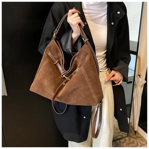 Detail van een grote bruine suède hobo tas met decoratieve leren riemen en gouden metalen gespen