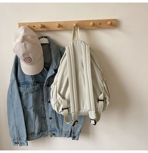 Close-up of a cream canvas backpack with adjustable straps on a wooden hook