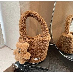 Detail of brown plush bucket bag with cute bear charm and woven label on a table