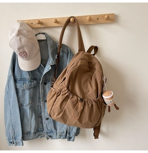 Detail of a brown nylon drawstring backpack with a plush coffee cup charm on wood hook