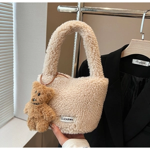 Close-up of beige plush bucket bag with CLEAR logo and brown teddy bear charm