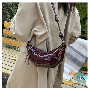 Detail of burgundy patent leather croissant bag with knotted strap and high gloss finish
