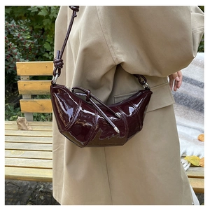 Detail of a dark burgundy patent leather croissant shoulder bag worn with a beige coat