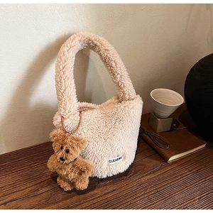 Close-up of cream fuzzy plush bucket bag with cute brown bear charm on wooden desk