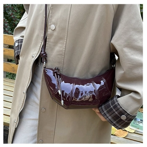 Detail of dark red glossy patent leather croissant bag worn with autumn style coat
