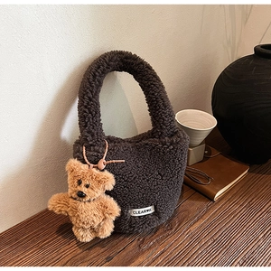 Detail of dark brown plush bucket bag with fuzzy bear charm and minimalist logo label