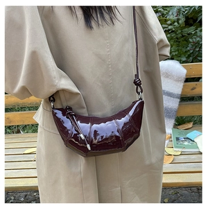 Close-up of deep red glossy patent leather croissant bag with elegant pleated texture detail