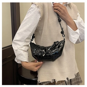 Detail of black glossy patent leather croissant bag with stylish knot strap on a model