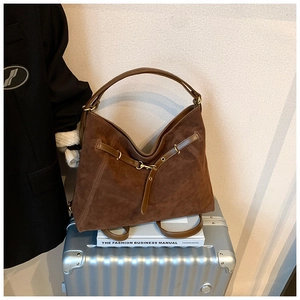 Detailed close-up of brown suede tote bag with leather strap and fashion book