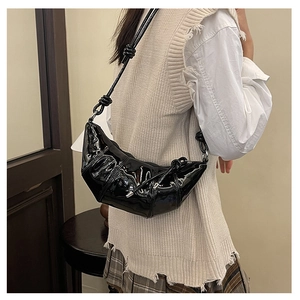Detail of black patent leather crescent bag featuring stylish ruched design and knotted strap