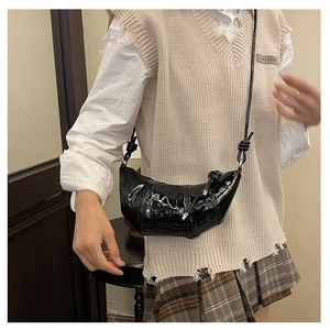 Detail of black patent leather croissant bag with knotted shoulder strap on a model