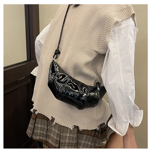 Detail view of high-gloss black patent leather dumpling bag worn on a beige knit vest