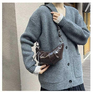 Close-up of dark brown patent leather croissant bag with knotted strap detail and metal ring