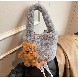 Close-up of fluffy grey-blue plush bucket bag with brand tag and cute brown bear charm