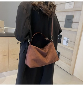 Sac sous le bras en cuir dépoli marron porté en bandoulière par un mannequin, style rétro