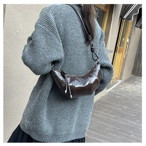 Detail of dark brown patent leather croissant bag with stylish knot strap on a model