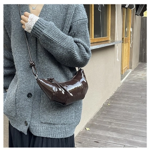 Detail of a dark brown glossy patent leather croissant bag with fine strap on a model