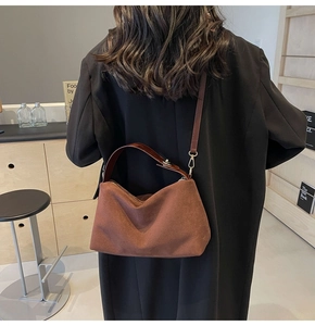 Gros plan d'un sac en daim marron rouge mat porté avec un blazer noir élégant
